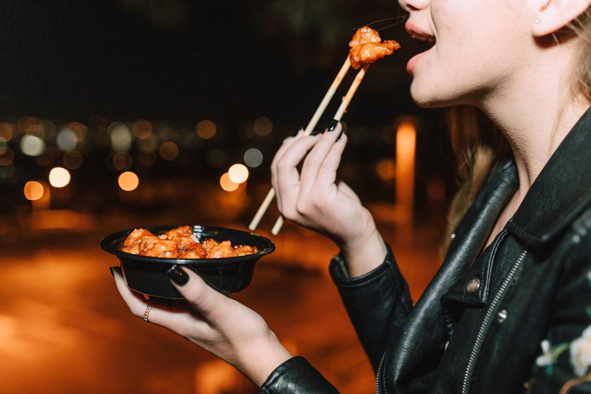 close up shot of a woman eating meat with orange sauce using chopsticks